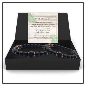 May include: A black gift box with a black and copper beaded bracelet inside. The box has a card inside with the message "To My Amazing Son." The card has a tropical leaf design.