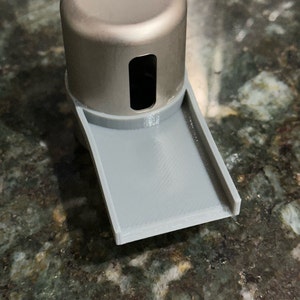 May include: A silver metal bottle stopper with a gray plastic drip tray. The stopper has a small hole in the top.