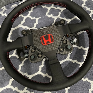 May include: Black leather steering wheel with red stitching and a carbon fiber center plate. The center plate features a red Honda logo and the text "ZESTEK" and "momo".