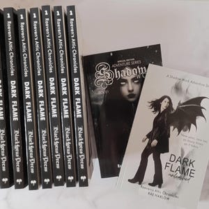 May include: Eight identical book spines titled Raeven's Attic Chronicles Dark Flame by Black Lotus Press, alongside two books. One book cover features a dark face, and the other shows a person with wings titled Dark Flame Unleashed by Rae Harlow.