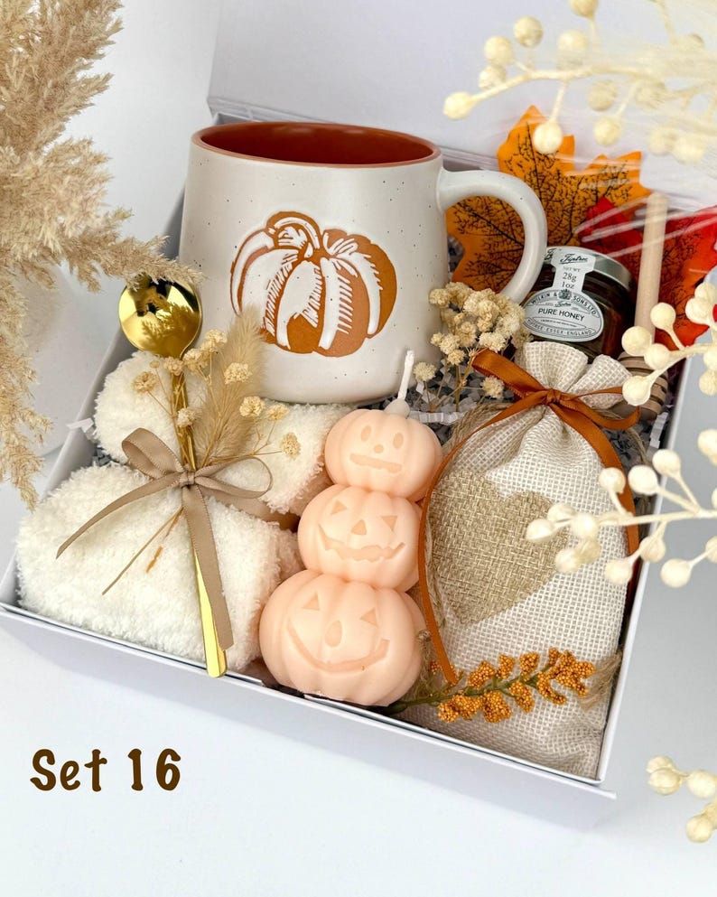 May include: A gift box labeled Set 16 containing a speckled ceramic mug with a pumpkin graphic, a stack of three pumpkin-shaped candles, a gold spoon, a small jar of honey, a wooden honey dipper, and a burlap pouch with a heart design.