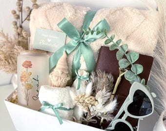 May include: A white gift box labeled "Set 1" filled with a beige blanket tied with a mint green ribbon, a candle with floral design, a small gnome candle, a notebook, sunglasses, and a card that says "Happy Birthday! Beautiful."