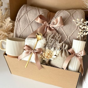 May include: A gift basket filled with a beige knitted blanket, a white mug with a brown base, a small white towel, a gold spoon, a small burlap bag, a white candle, and dried flowers. All items are tied with a satin ribbon. The text "Set 11" is at the bottom.