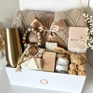 K&ouml;nnte beinhalten: Eine Geschenkbox mit Pflegeprodukten. Sie enth&auml;lt eine beige Decke, einen goldenen Becher, ein Perlenarmband, Haferflocken-Seife, Badesalz, Seife in Teddyb&auml;rform und eine Schleife. Auf der Box steht "Set 9".
