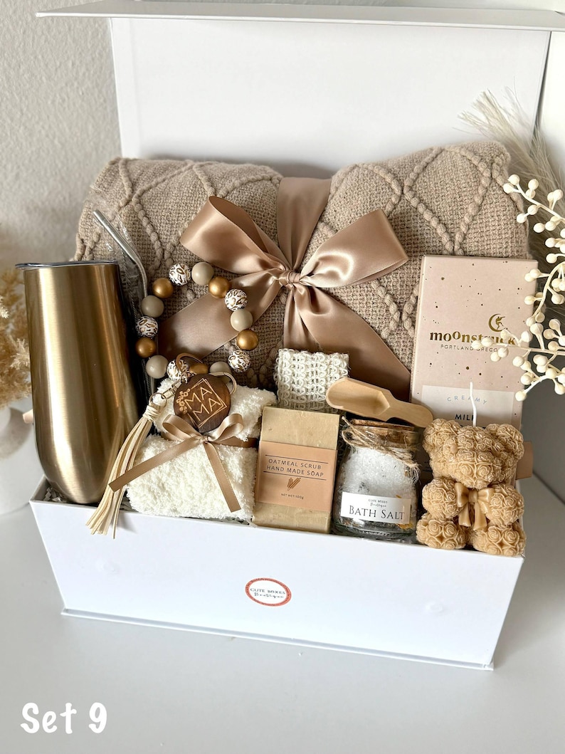 K&ouml;nnte beinhalten: Eine Geschenkbox mit Pflegeprodukten. Sie enth&auml;lt eine beige Decke, einen goldenen Becher, ein Perlenarmband, Haferflocken-Seife, Badesalz, Seife in Teddyb&auml;rform und eine Schleife. Auf der Box steht "Set 9".