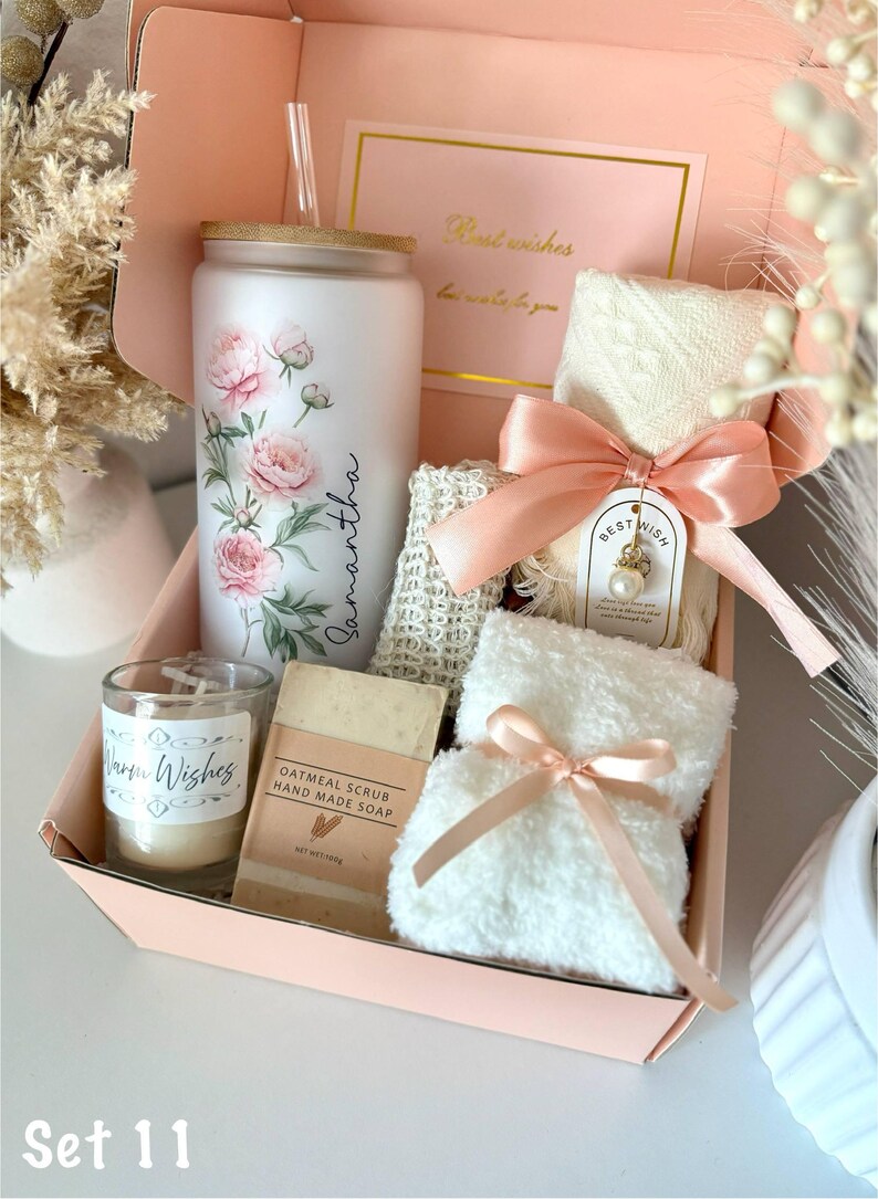 May include: A gift set in a pink box includes a white tumbler with pink floral design and the name "Samantha", a candle, soap, washcloths, and a card that says "Best wishes". The set is tied with a pink ribbon.