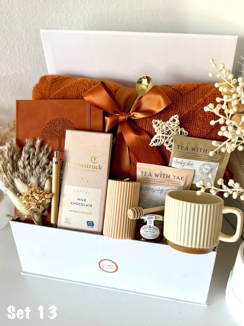 Puede incluir: Una caja de regalo llena de varios art&iacute;culos en tonos c&aacute;lidos. Incluye una manta color &oacute;xido, un diario, chocolate, t&eacute;, una taza, una vela y miel. Una cuchara dorada y un lazo decorativo a&ntilde;aden un toque de elegancia. La caja est&aacute; etiquetada "Set 13".