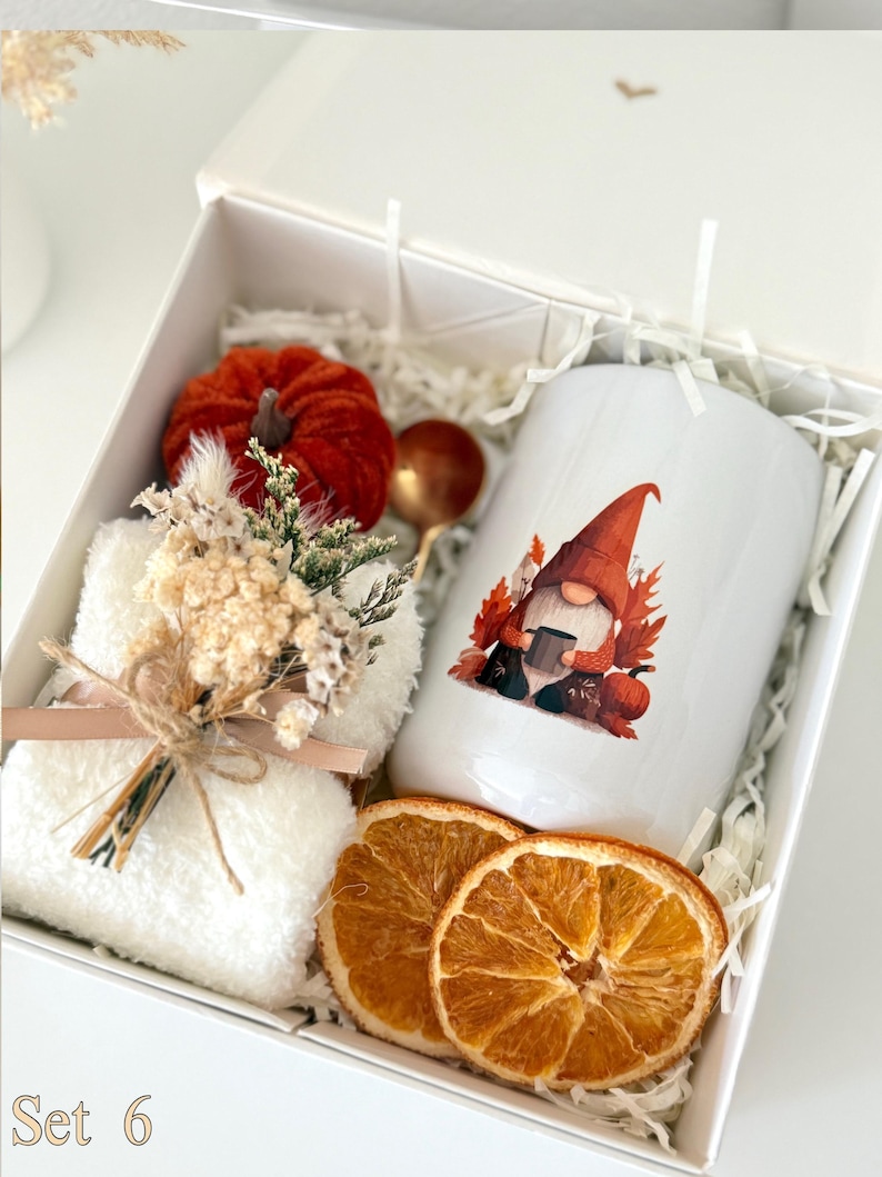 May include: A white gift box containing a white mug with a gnome graphic, a small red velvet pumpkin, a gold-toned spoon, a white fuzzy cloth, a dried floral bouquet tied with twine, and two dried orange slices, with the text Set 6 visible.