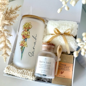 May include: A white gift box contains a frosted glass tumbler with a floral design and the name "Sarah", a jar of bath salt, a bar of oatmeal soap, two white washcloths tied with a gold ribbon, and a small wooden spoon. The text "Set 12" is at the bottom.