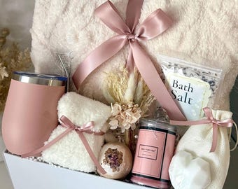 May include: A gift set containing a cream-colored faux fur blanket tied with a pink ribbon, a pink tumbler with a straw, a small white plush item, a dried floral arrangement, a bath bomb, a candle labeled ONLY FOR YOU, bath salts, and a small pouch.