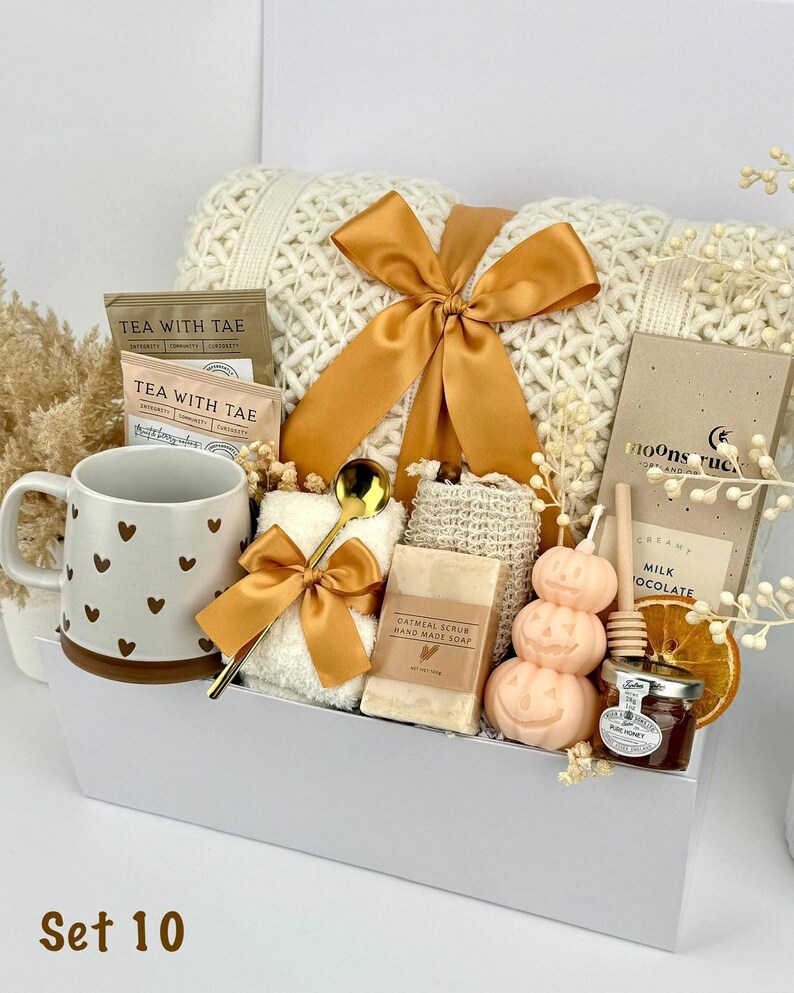 May include: A gift set containing a white knit blanket with a gold ribbon, a mug with brown hearts, two Tea With Tae packets, a gold spoon, a white washcloth, oatmeal soap, a pumpkin candle, a honey jar with a dipper, and a chocolate bar.