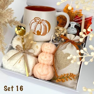 May include: A gift box labeled Set 16 containing a speckled ceramic mug with a pumpkin graphic, a gold spoon, white fuzzy socks, a stack of three peach-colored pumpkin candles, a small jar of honey, a wooden honey dipper, and a burlap pouch.