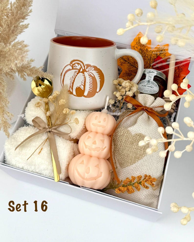 May include: A gift box labeled Set 16 containing a speckled ceramic mug with a pumpkin graphic, a gold spoon, white fuzzy socks, a stack of three peach-colored pumpkin candles, a small jar of honey, a wooden honey dipper, and a burlap pouch.