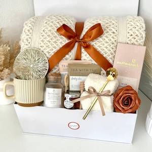 Puede incluir: Una caja de regalo blanca llena de una manta de punto color crema atada con una cinta color &oacute;xido. Tambi&eacute;n contiene una taza, sal de ba&ntilde;o, miel, un osito de peluche, una tableta de chocolate, una cuchara dorada, un posavasos y una rosa.