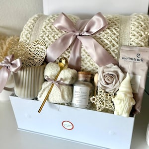 Puede incluir: Una caja de regalo blanca llena de art&iacute;culos de cuidado personal. Incluye una manta de punto color crema atada con una cinta malva, sales de ba&ntilde;o, una vela, un osito de peluche, una rosa y un gnomo. La caja est&aacute; etiquetada como "Set 15".