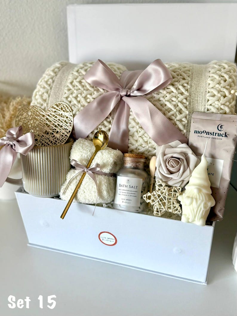 Puede incluir: Una caja de regalo blanca llena de art&iacute;culos de cuidado personal. Incluye una manta de punto color crema atada con una cinta malva, sales de ba&ntilde;o, una vela, un osito de peluche, una rosa y un gnomo. La caja est&aacute; etiquetada como "Set 15".