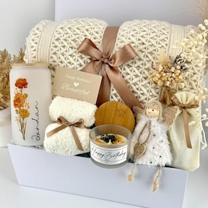 May include: A gift set containing a cream-colored knit blanket tied with a brown ribbon, a frosted glass tumbler with floral art and the name Jordan, a small candle with a bamboo lid, a plush angel ornament, and a small pouch, labeled Set 4.