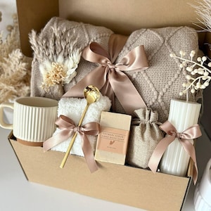 May include: A gift basket filled with a beige knitted blanket, a white mug, a small towel, a bar of oatmeal scrub soap, a small burlap bag, and a white candle. The items are tied with satin ribbons. The text "Set 10" is at the bottom.