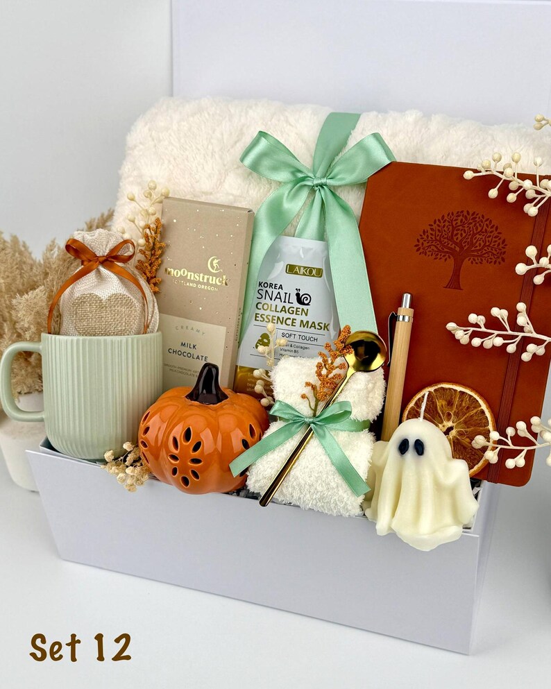 May include: A gift set in a white box containing a ribbed light green mug, a Moonstruck milk chocolate bar, a Laikou snail collagen essence mask, a brown notebook with a tree design, a bamboo pen, a pumpkin-shaped item, and a ghost-shaped candle.