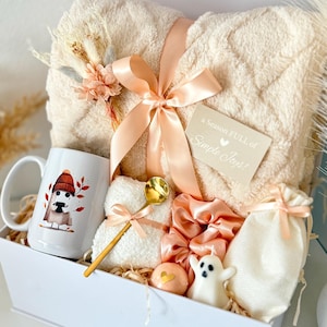 May include: A gift box containing a cream-colored fuzzy blanket tied with a peach ribbon, a white mug with a ghost illustration, a gold spoon, a peach scrunchie, a ghost-shaped candle, a small drawstring bag, and a card reading a season FULL of Simple Joys!