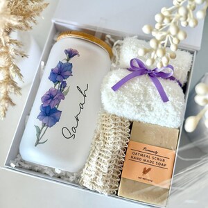 May include: A white gift box containing a glass tumbler with a floral design and the name "Sarah", a white washcloth with a purple ribbon, a loofah, and a bar of oatmeal scrub soap. The set is labeled "Set 10".
