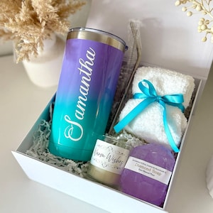May include: A gift set in a white box, featuring a gradient purple and teal tumbler with the name "Samantha", a small candle, a bar of purple soap, and a white washcloth tied with a teal ribbon. The box is filled with shredded paper.