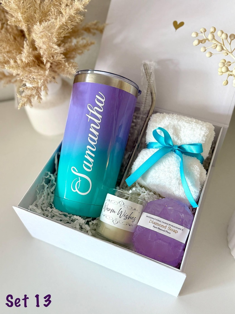 May include: A gift set in a white box, featuring a gradient purple and teal tumbler with the name "Samantha", a small candle, a bar of purple soap, and a white washcloth tied with a teal ribbon. The box is filled with shredded paper.