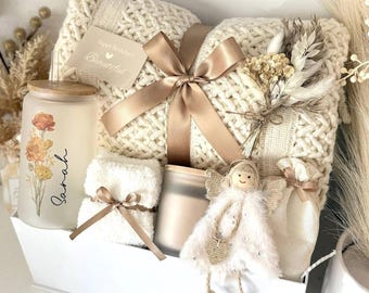 May include: A white gift box filled with a cream-colored knitted blanket tied with a brown satin ribbon. The box also contains a candle, a small towel, a decorative angel, and a small bag. The candle has a floral design and the name "Sarah" on it. The box is labeled "Set 4".