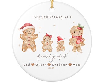 May include: A white ceramic Christmas ornament with a gold string. The ornament features a watercolor illustration of a gingerbread family of four, with text that reads "First Christmas as a family of 4".