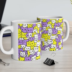 May include: Two white ceramic mugs with a pattern of purple and yellow cartoon cats. The mugs are on a wooden table.