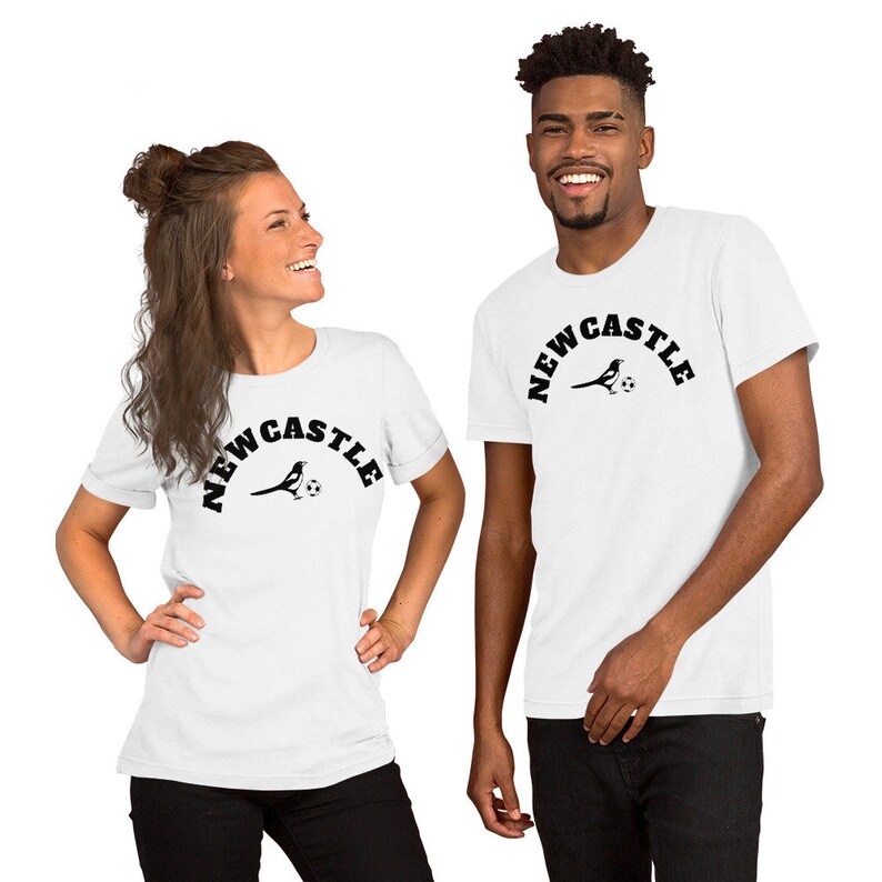 May include: Two people wearing white t-shirts with a black graphic of a magpie holding a football and the text "NEWCASTLE".
