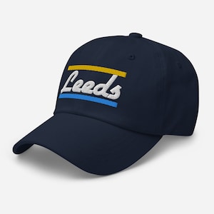 Puede incluir: Una gorra de béisbol azul marino con un logotipo "Leeds" bordado en blanco y rayas amarillas y azules.