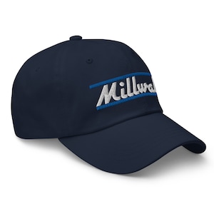 Może przedstawiać: Czapka bejsbolowa w kolorze granatowym z haftowanym białym logo z napisem "Milwaukee" z niebieskim paskiem nad tekstem.