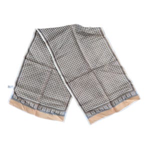 May include: A rectangular scarf with a geometric pattern in shades of brown, white, and blue. The scarf has a tan border and a repeating square design. The scarf is made of a lightweight material.