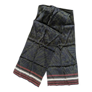 May include: A dark green scarf with a repeating pattern of dark blue shapes and a striped border in red, white, and gray. The scarf is folded and draped, showcasing its design and texture.