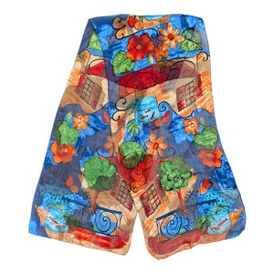 May include: A colorful scarf with a whimsical design featuring orange and red flowers, green trees, and blue fish tanks. The scarf has a blue background with a mix of orange, red, and green accents.