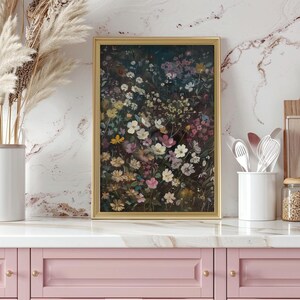 May include: A framed print of a floral arrangement featuring a variety of flowers in shades of pink, purple, and white. The flowers are arranged in a dense cluster, creating a vibrant and colourful display. The print is framed in a gold frame and is hanging on a white marble wall.