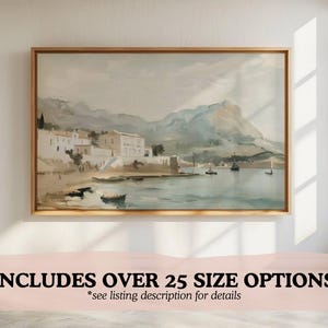 May include: A watercolor painting of a coastal town with white buildings and boats in the water. The painting is framed in a light wood frame.