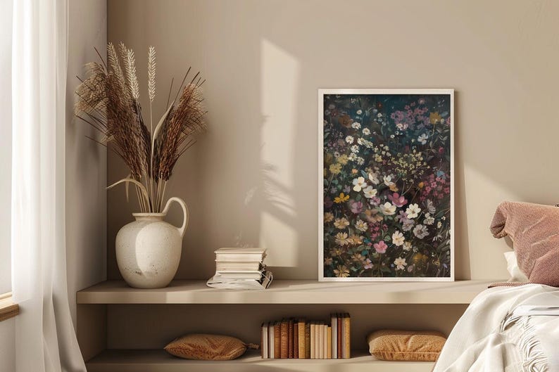 May include: A framed print of a floral arrangement featuring a variety of white, pink, and purple flowers on a dark background. The print is hanging on a beige wall above a shelf with books and a vase of dried grasses.