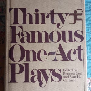Może przedstawiać: Książka w twardej oprawie zatytułowana Thirty Famous One-Act Plays, pod redakcją Bennetta Cerfa i Vana H. Cartmella, wydana przez Modern Library. Okładka jest jasnobeżowa z ciemnofioletowym tekstem i cienką fioletową ramką wokół tytułu.