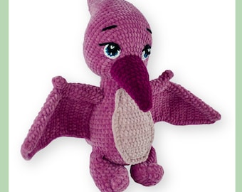 May include: A handmade, plush pterodactyl toy in shades of purple, with a lighter beige chest. The crochet dinosaur has large, blue eyes, a dark purple beak, and outstretched wings. The toy is designed to stand upright.