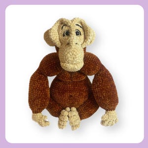 Puede incluir: Un juguete de peluche de mono marrón y beige tejido a crochet en posición sentada. El mono tiene una cabeza grande con una cara marrón y ojos negros.