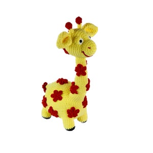 Puede incluir: Un juguete de peluche de jirafa de color amarillo tejido a crochet con detalles de flores rojas. La jirafa tiene una cara sonriente y está de pie sobre un fondo blanco.