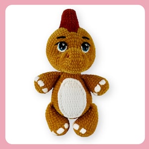 May include: A handmade crochet dinosaur plush toy in shades of brown, with a white belly and white accents on its feet and hands. The dinosaur has blue eyes and a red crest on its head. The toy is designed with a soft, textured appearance.