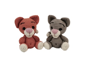 Peut inclure: Deux animaux en peluche crochetés, l'un orange et l'autre gris, assis côte à côte. Les deux ont un nez rose et des yeux noirs.