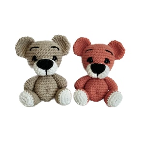 Puede incluir: Dos osos de peluche tejidos a crochet, uno en beige y otro en melocotón, sentados uno al lado del otro. Ambos osos tienen ojos y narices negros y pies blancos.