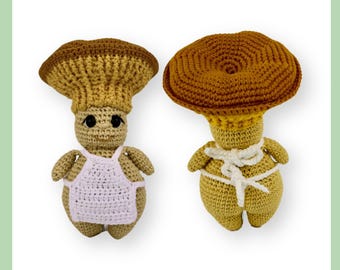 May include: Two crocheted mushroom plushies. One is wearing a pink apron and the other has a white ribbon tied around its waist.
