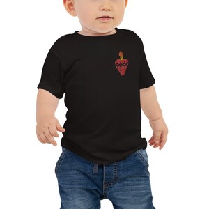 May include: Black baby t-shirt featuring a red heart design with a flame at the top. The heart has a textured appearance. The t-shirt is short-sleeved and made of a soft material. The baby is wearing blue jeans.