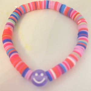 May include: A colorful beaded bracelet with a purple smiley face charm. The bracelet is made of small, round beads in various shades of pink, blue, red, and yellow.