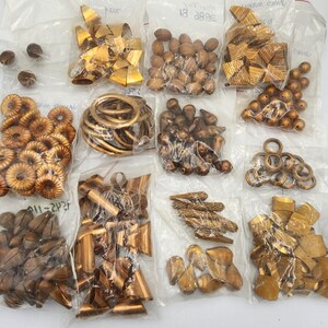 May include: Assortment of gold-colored metal beads and charms in individual plastic bags. The bags are labeled with the names of the different types of beads and charms.  The beads and charms are in various shapes and sizes.